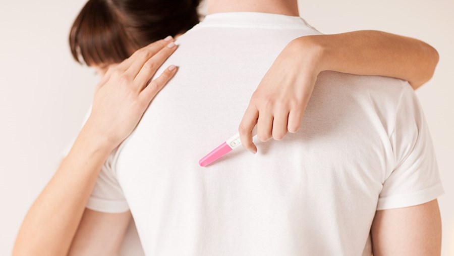 Paar umarmt sich und Frau hält Schwangerschaftstest in der Hand.