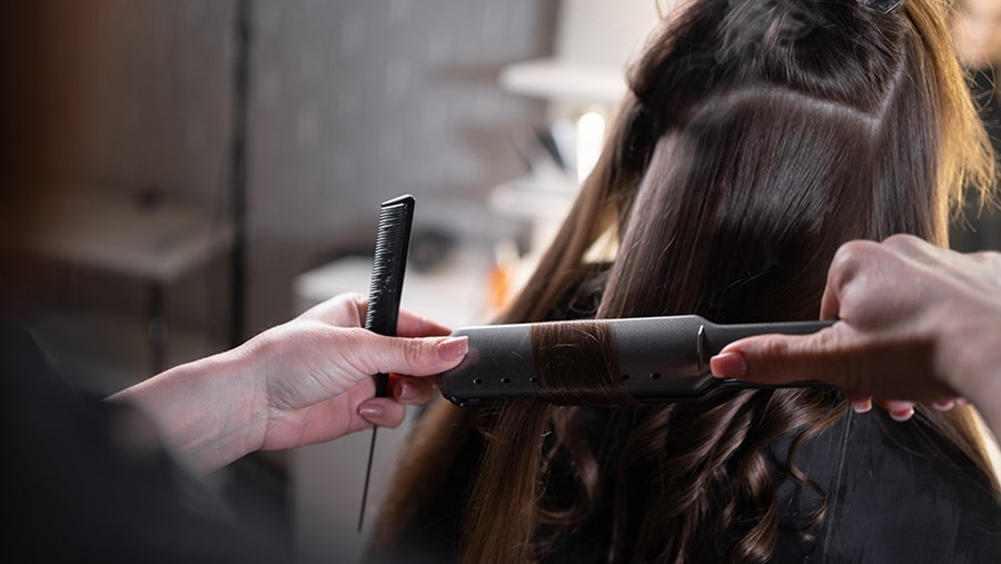 Frau macht Locken mit dem Glättseisen in die Haare einer anderen Frau